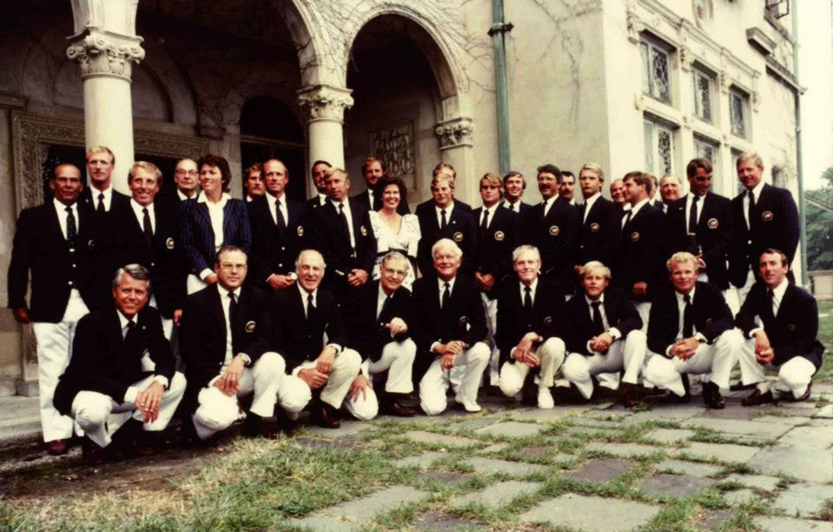 Group of men in formal attire posing outdoors in front of a classical building.
