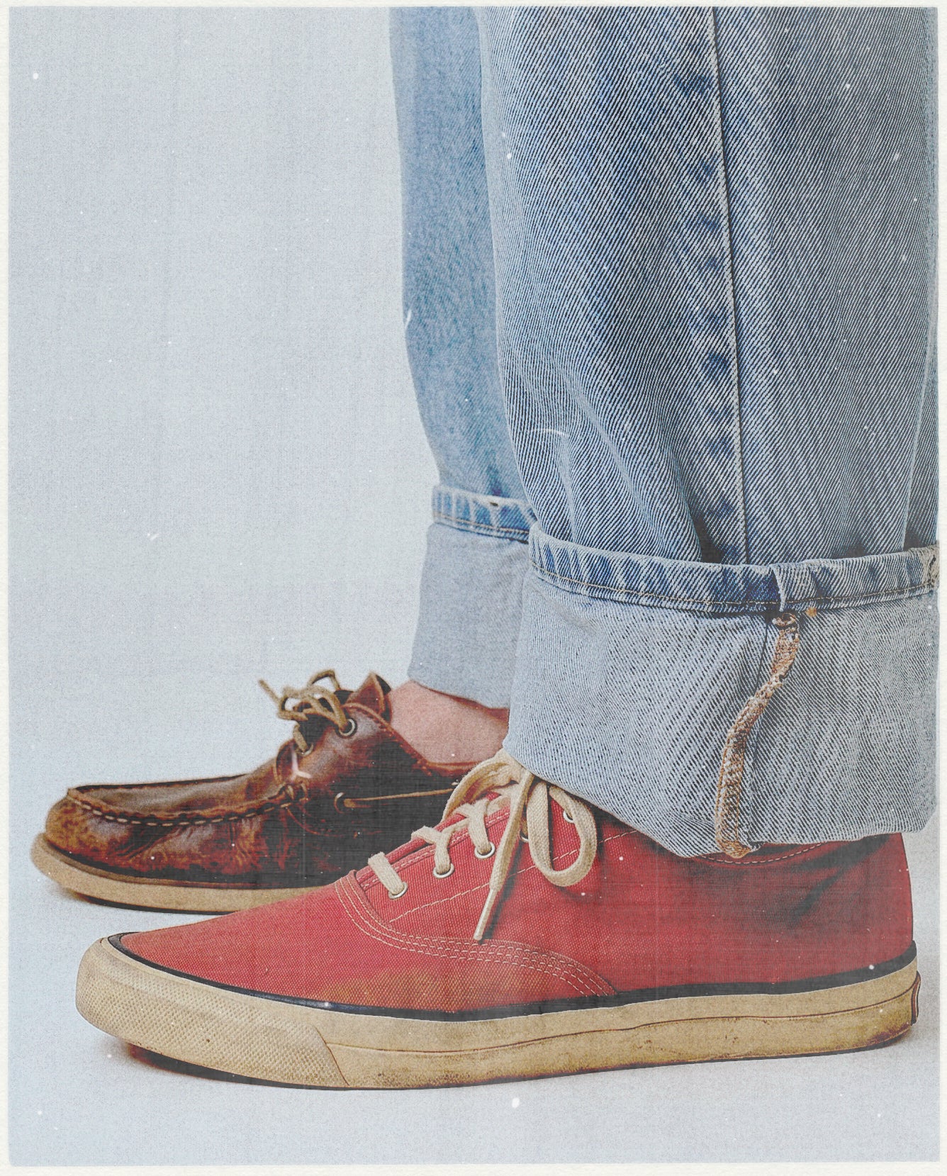 Red sneakers worn with rolled-up blue jeans on a light gray background