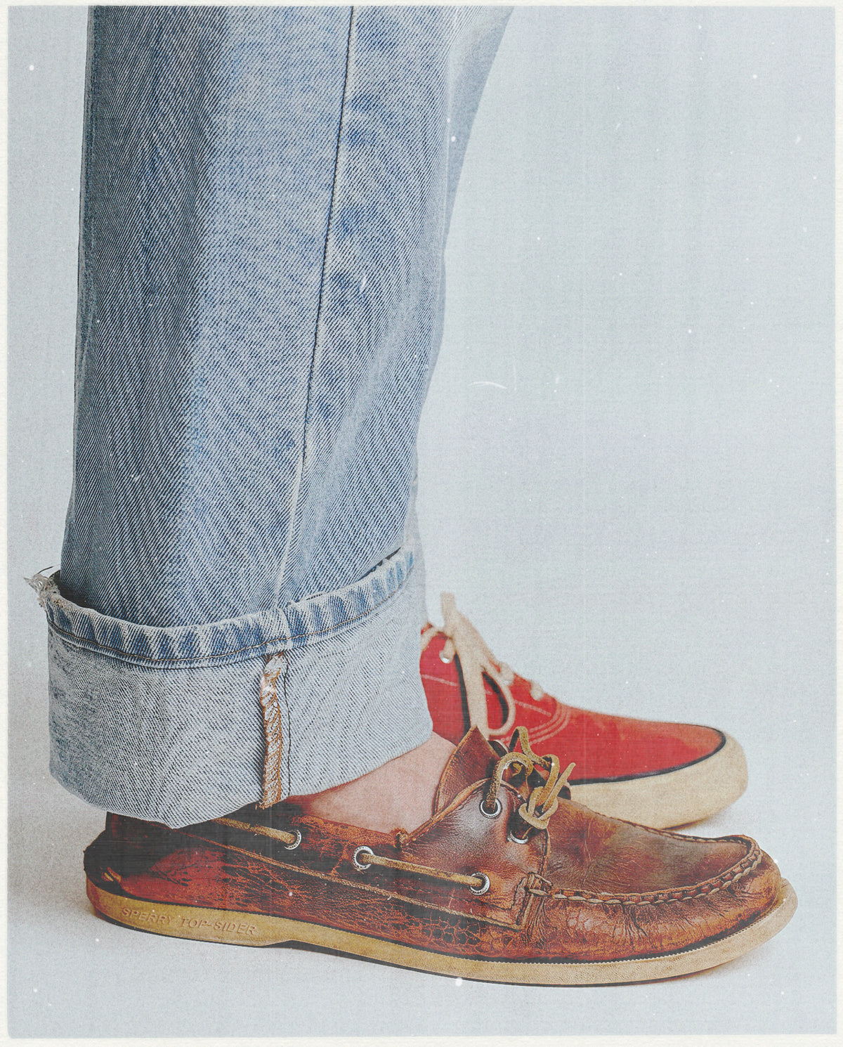 Brown leather shoes worn with rolled-up jeans on a light gray background