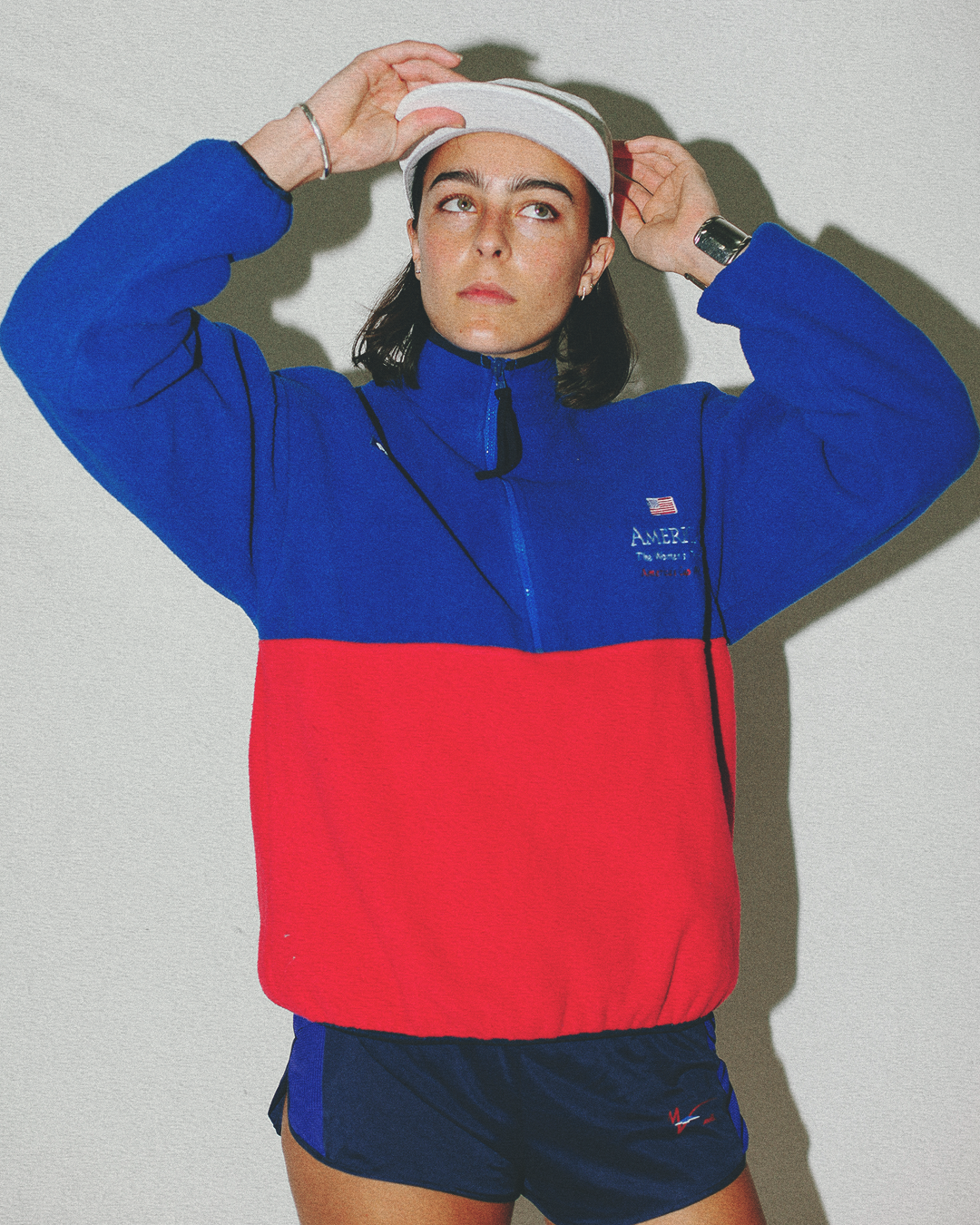 Person wearing a blue and red jacket with a white cap on a plain background