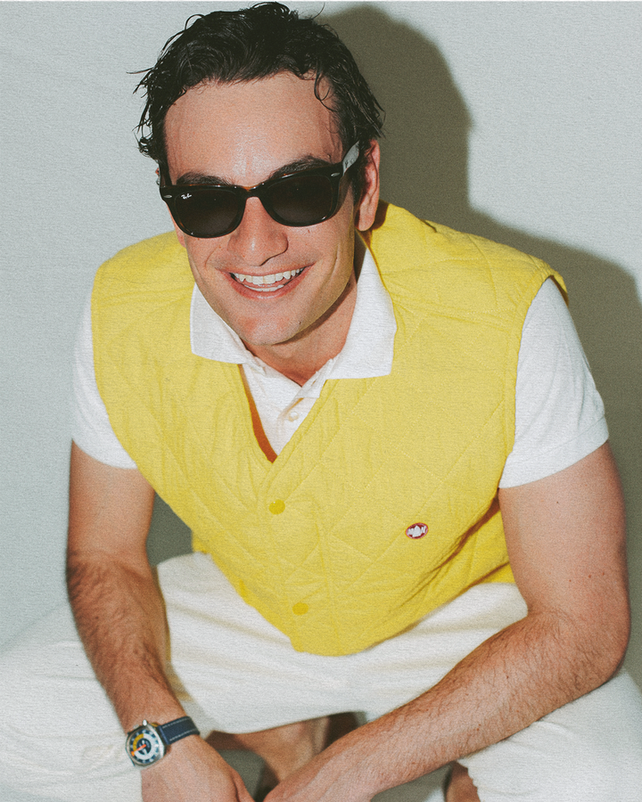 Man wearing a yellow vest and sunglasses against a plain background