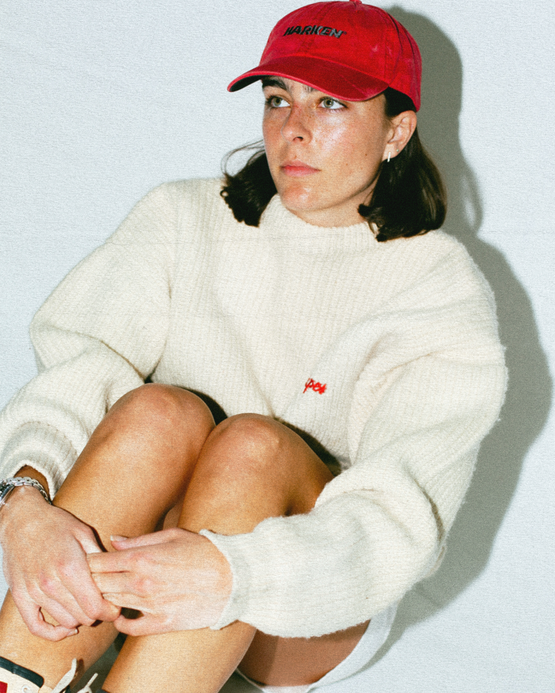 Person wearing a red cap and white sweater sitting against a light background