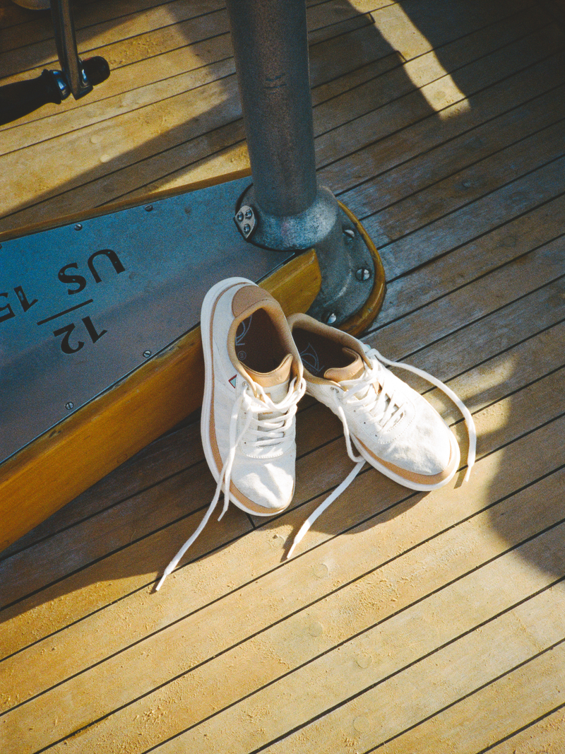 A pair of white canvas high-top sneakers with tan lining and white laces, resting on a wooden deck next to a metal post.
