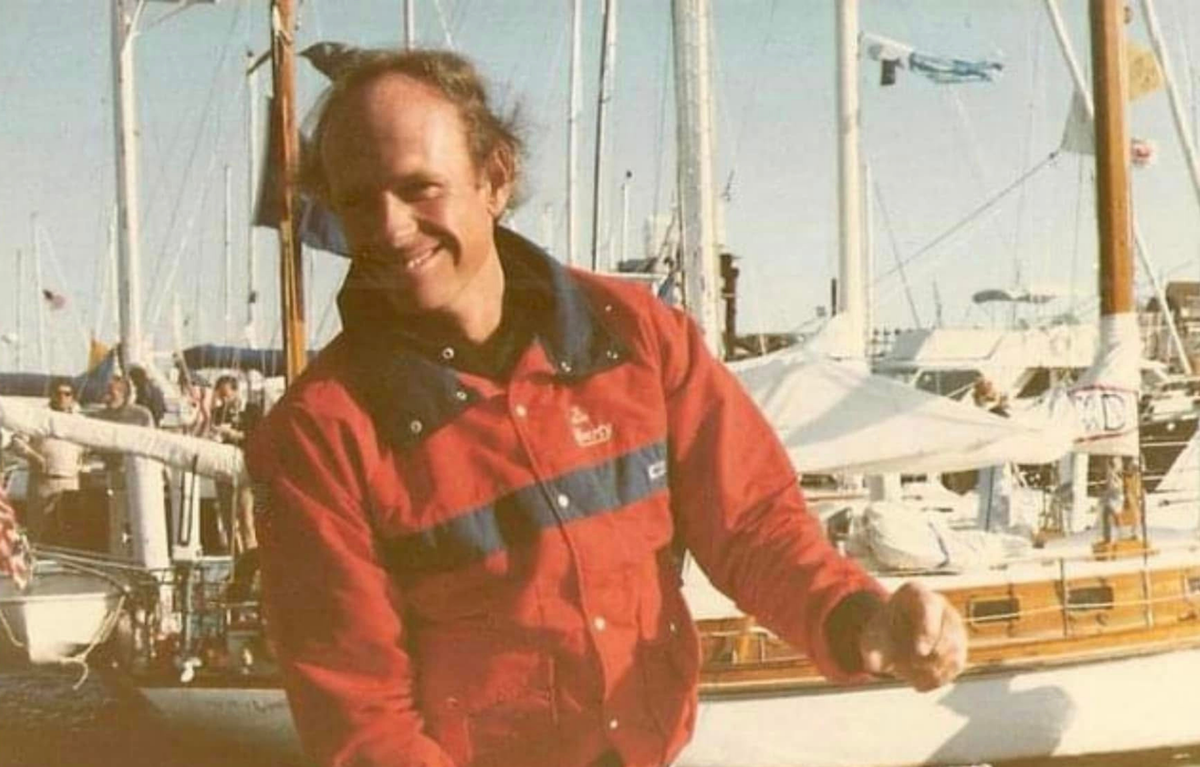 Man in a red jacket standing in front of sailboats
