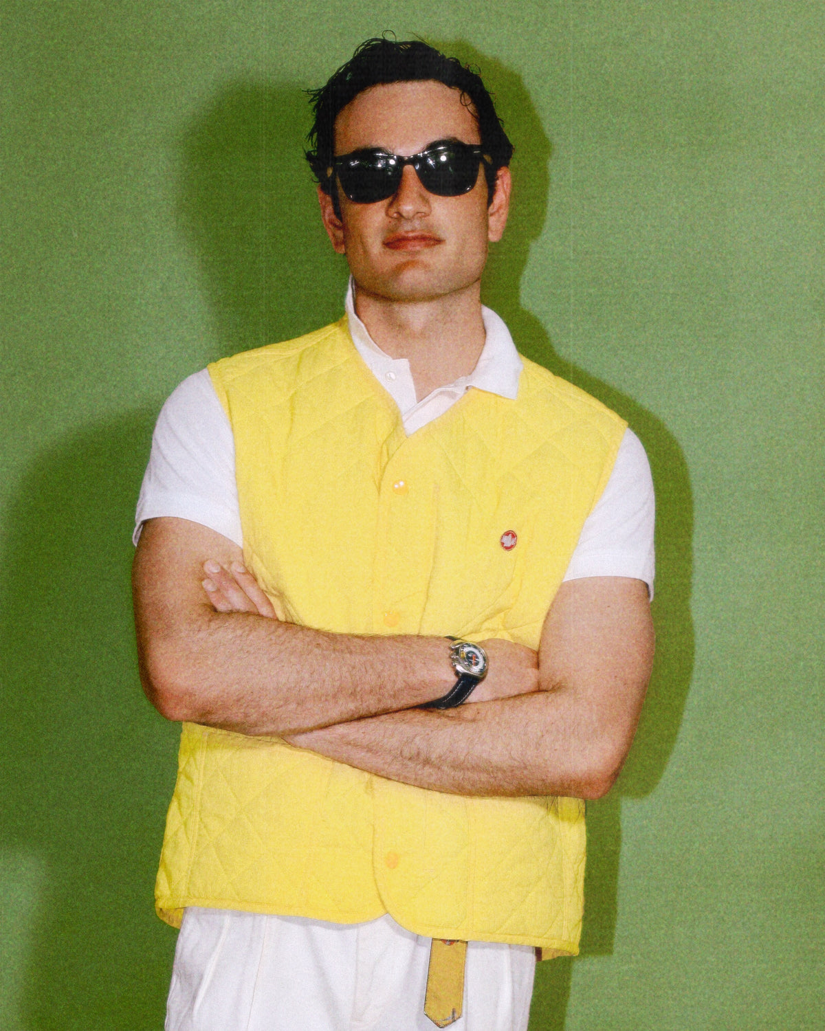 Man wearing a yellow Il moro vest over a white shirt with sunglasses against a green background