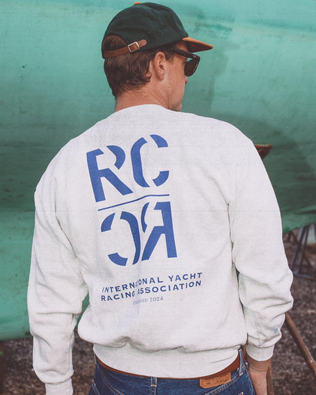 Person wearing a sweatshirt with 'RC International Yacht Racing Association' text on the back, standing against a green background.