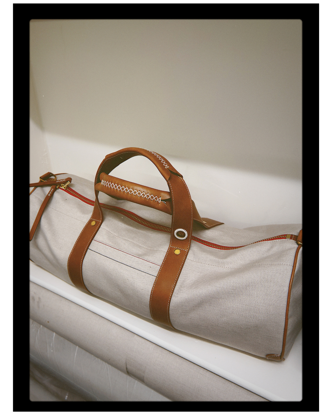 Beige duffel bag with brown leather straps on a white surface