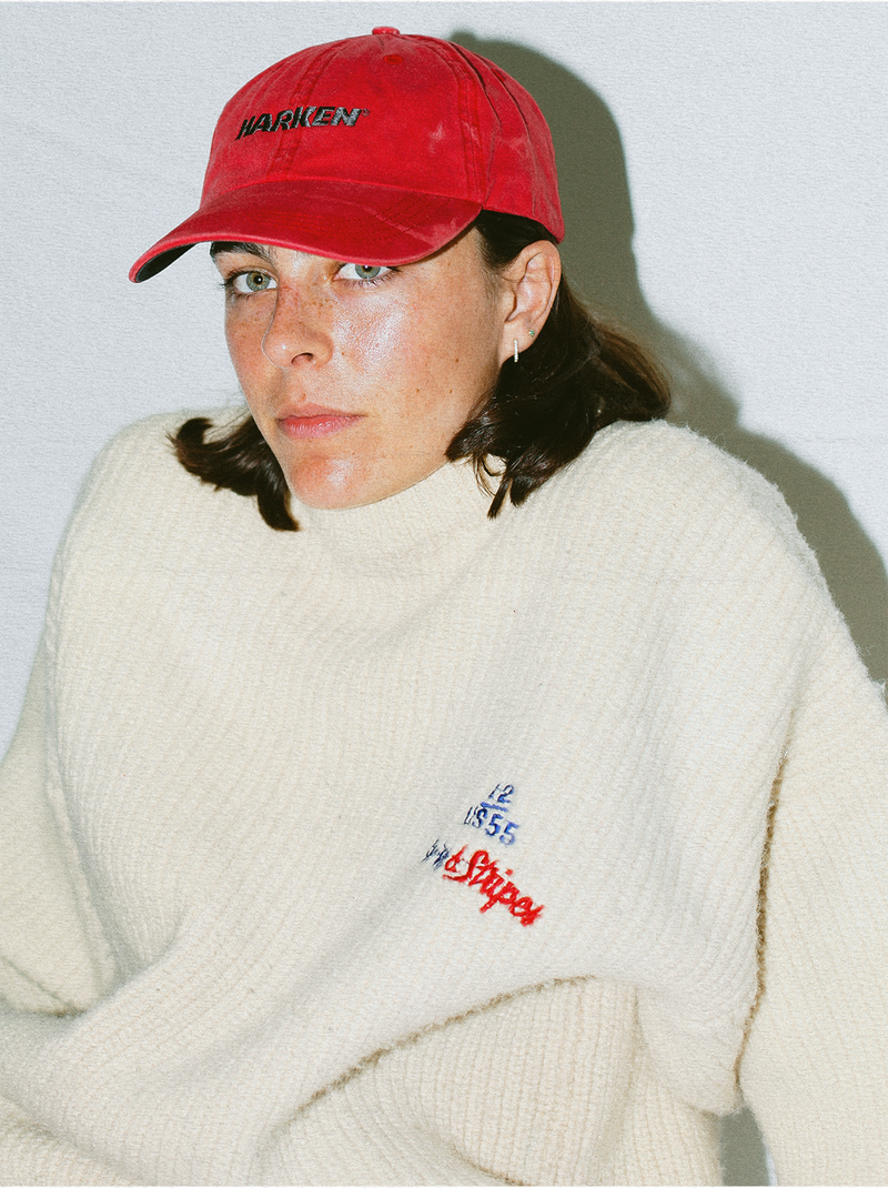 Person wearing a red cap and white sweater with embroidered text against a plain background