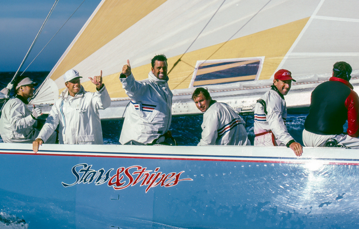 Sailboat with crew members on a sunny day, featuring the 'Stars & Stripes' logo.